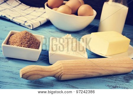 some ingredients for preparing cookies or a cake, such as milk, eggs, flour, butter and brown sugar on a blue rustic wooden surface, with a filter effect