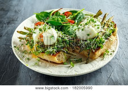 Healthy Breakfast Smashed Avocado, asparagus and poached egg on grilled toasts for breakfast served with salad and plum tomatoes.