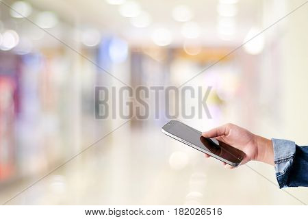 Hand using smart phone over blur store with bokeh light background business and technology concept digital marketing seo e commerce lifestyle social media network