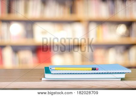 Notebook paper and pencil on table over blur book store background with copy space for display montage education concept