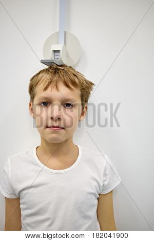 Boy stands at stadiometer near wall.
