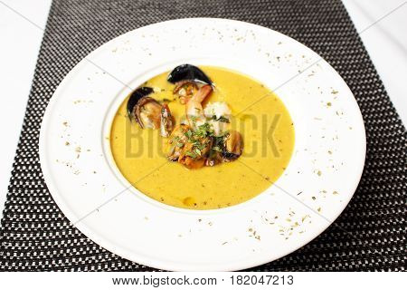 Soup-puree pumpkin with shrimps in a clay bowl with parsley On a black napkin