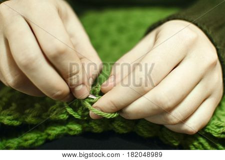 Women's hands knitting green scarf by needles