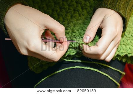 Women's hands knitting green scarf by needles