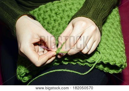 Women's hands knitting green scarf by needles