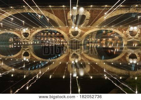 Pont Neuf beautifully illuminated on dark night across Garrone River Toulouse France.