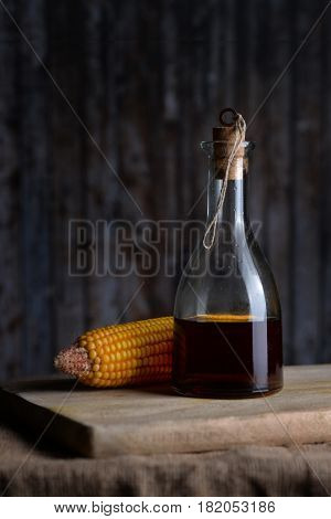 Salad oil in a glass bottle and corn on a background of blue board.