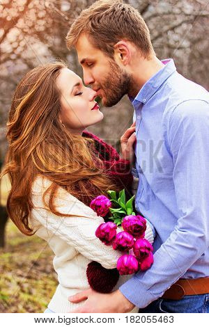 Happy Couple Together. Portrait Of Bearded Man Kissing His Lovely Girlfriend With Flowers On The Gar