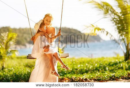 happy family at beach. mother shook child on swing in summer and laughs