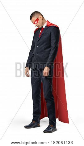 A sad businessman in a superhero red cape standing with his shoulders slumped and looking down. Profit and loss. Unexpected problems. Business pitfalls.