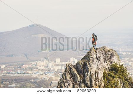A young climber looking out of the top of a steep cliff against the background of the city and mountains