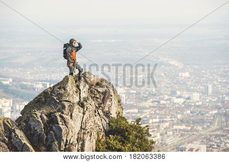 A young climber looking out of the top of a steep cliff against the background of the city and mountains