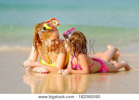 Happy family mother and chid daughter in masks for swimming on the beach in summer