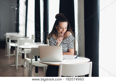 Photo of pretty woman fiddling with pen and thinking over a subject while sitting in some coffee shop with her laptop