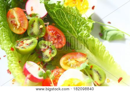 Overhead of lettuce leaves with cherry tomatoes baby kiwi fruits radishes and boiled eggs with red pepper flakes