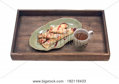 Delicious cheese blintz and raspberry syrup on green plate with cup of tea and wooden vintage tray isolated on white background
