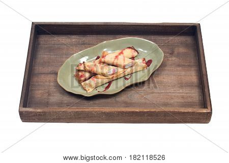 Delicious cheese blintz with raspberry syrup on green plate and wooden vintage tray