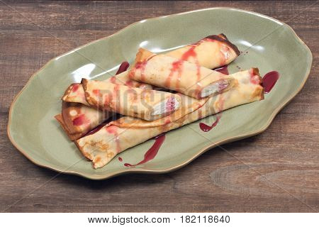 Delicious cheese blintz with raspberry syrup on green plate and wooden vintage tray