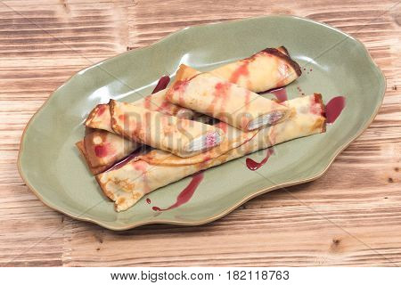 Delicious cheese blintz with raspberry syrup on green plate and wooden vintage tray