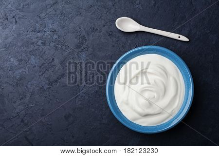 Greek yogurt in blue bowl on black table top view. Flat lay.