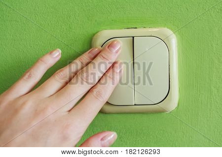 Female hand pressing two keys beige light switch mounted on green wall