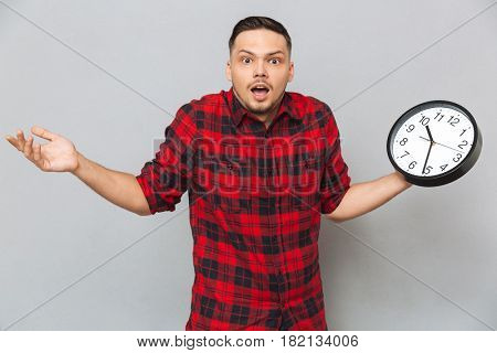 Incomprehensible man in shirt holding clock and looking at the camera over gray background