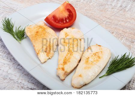 Slices of roasted chicken breast and tomato on white plate.