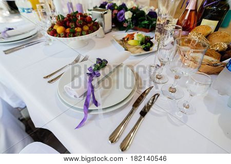 White napkin with purple flowers on a white empty plate on a dining table. Table setting. Table served for wedding banquet close up view