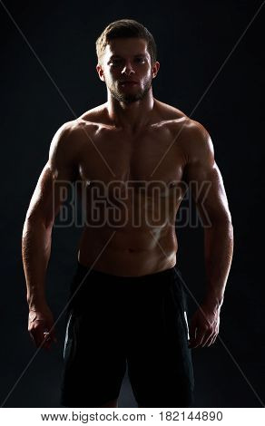 Vertical studio shot of a silhouette of a muscular male athlete posing shirtless on black background fitness gym anonymous mysterious incognito sportsman lifestyle confidence concept.