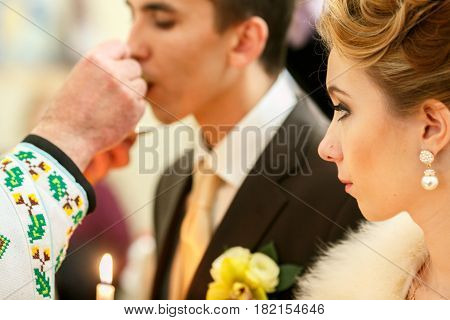 Bride Looks At A Groom While He Kisses A Wedding Ring Helb By A Priest