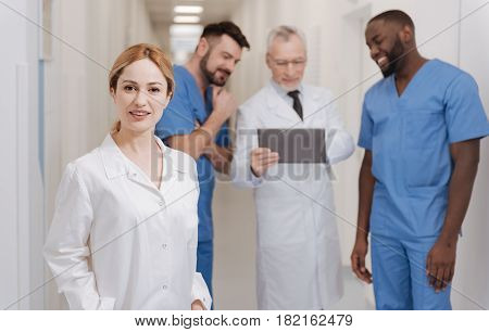 Happy to be the part of collective . Beautiful young smiling nurse working in the hospital and smiling while other colleagues using gadget in the background