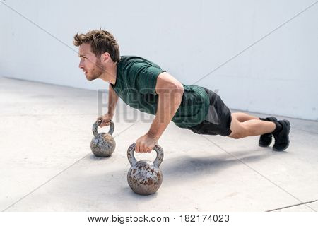 Fitness man strength training body core doing push-ups holding on kettlebells bodyweight floor exercises at outdoor gym.