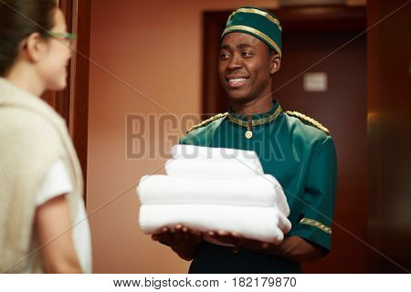 Happy hotel servant giving clean towels to one of guests