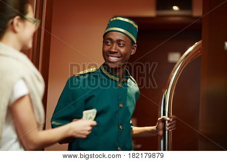 Young guest of hotel giving porter money for his help