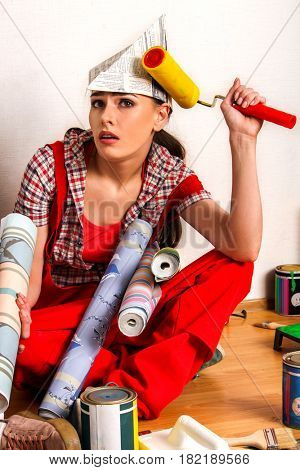 Repair home woman holding paint roller for wallpaper. Tired and frustrated female in newspaper cap renovation apartment. Paint bank and roll paper background on isolated.