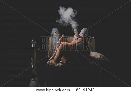 traditional arabic kalian pretty woman with sexy back and body in jeans sitting on eastern chair with shisha bong naked girl smoking hookah on black background