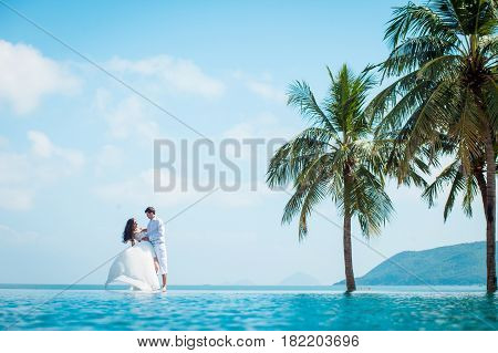 Newly married couple after wedding in luxury resort. Romantic bride and groom relaxing near swimming pool and sea. Honeymoon. Tropical country.