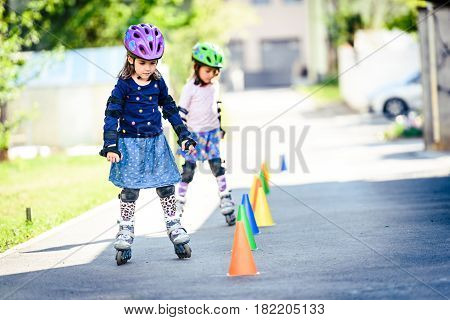 Children Learning To Roller Skate On The Road With Cones.