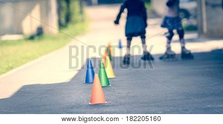 Children Learning To Roller Skate On The Road With Cones.