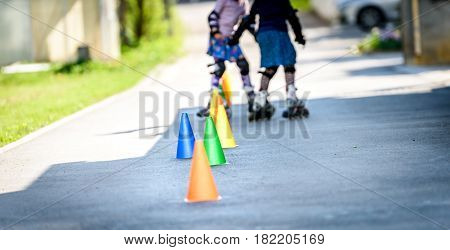 Children Learning To Roller Skate On The Road With Cones.