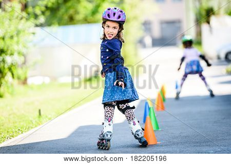 Children Learning To Roller Skate On The Road With Cones.