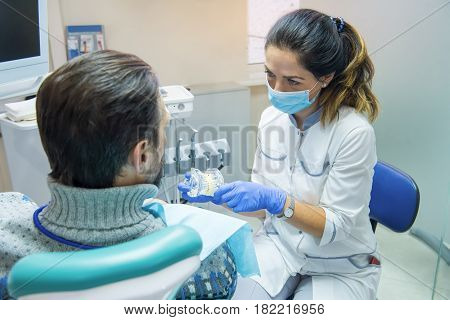 Dentist holding artificial teeth. Stomatologist with her patient. Benefits of tooth implants.