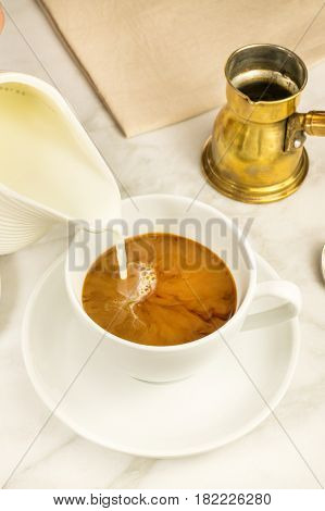 Milk poured into a cup of coffee, with a vintage coffee pot in the background. Selective focus, place for text