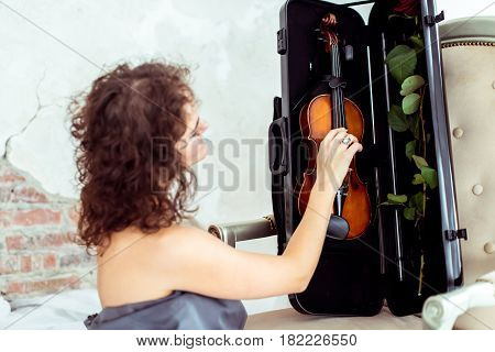 Side view beautiful womansitting near chair and touching violin in the case in studio