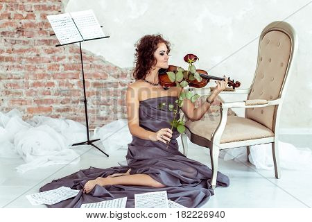 beautiful woman sitting on the floor near a chair and playing the violin bow rose instead in studio