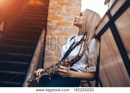 Profile portrait young attractive girl in white shirt with a saxophone - outdoor in old town. Sexy young woman with sax thinking about something.