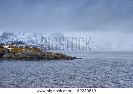 Travel and Tourism Concepts. One Separate House on Seashore Coastline in Norway Against Mountains Covered With Snow.Horizontal Image