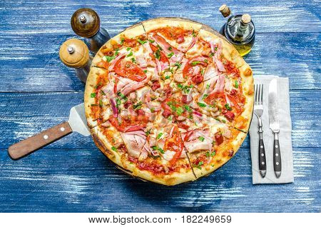 Round pizza with meat tomatoes and herbs cutlery and spices
