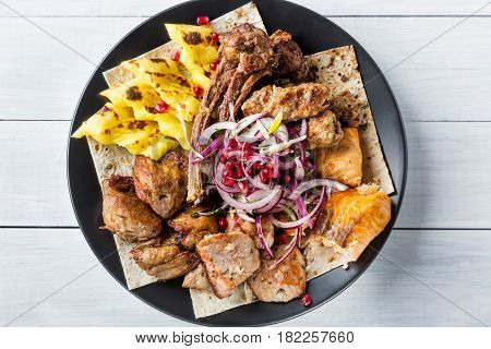 Lyulya kebab shish kebab grilled salmon fish onion and pomegranate grains on black plate and white wooden table. Top view.
