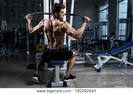 Fitness man with a naked torso trains on cable machine in the gym